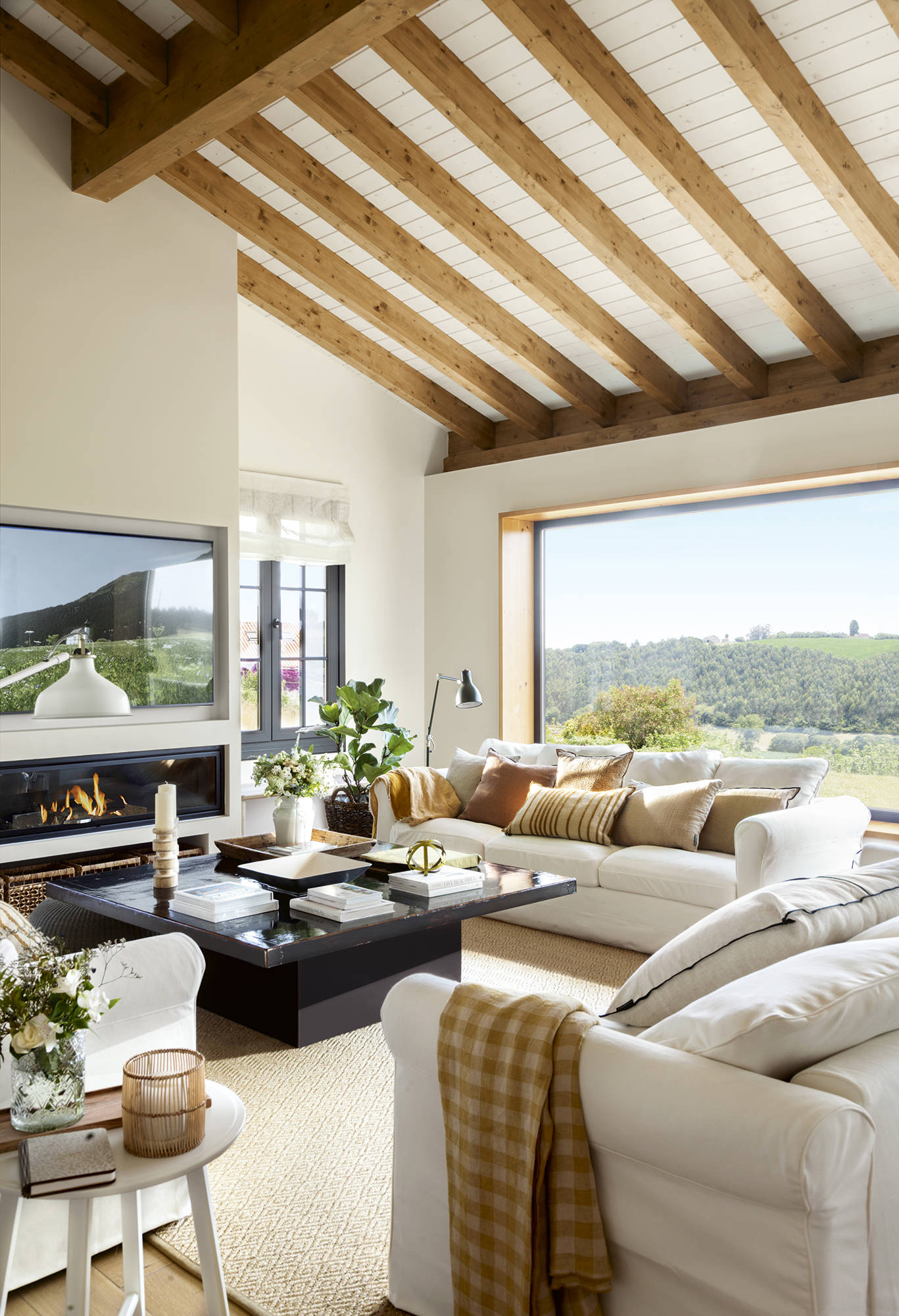 Salón con sofás blancos, chimenea, mesa de centro de madera y vigas. 